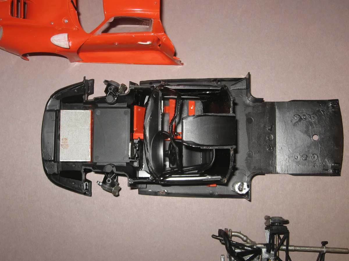 A Tamiya 911 GT1 car kit on a table, an orange body above a black chassis whose rear shows filled pin marks, still rough before sanding