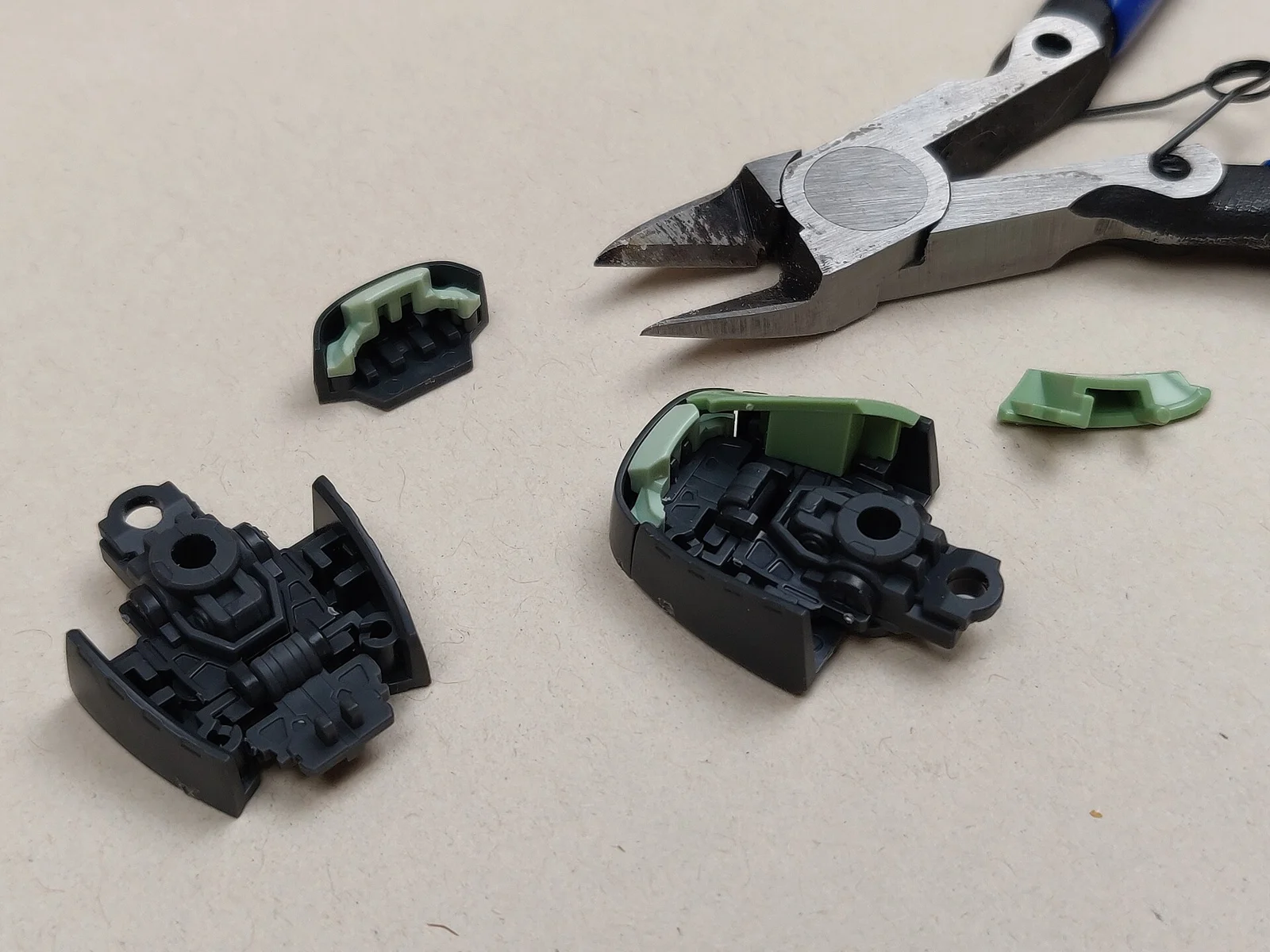 Two disassembled black and green Real Grade Zaku II foot units with their inner hinge parts, a loose green armor panel and a pair of nippers on a beige surface